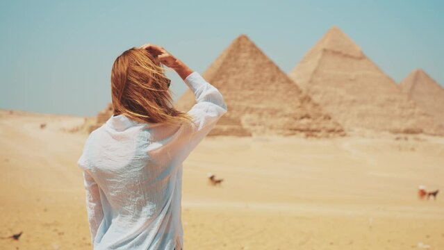 Tourist woman in takes photo on smartphone of Great Giza pyramids in Cairo Egypt enjoys attraction of world UNESCO ancient heritage, back view. Tourism travel wanderlust journey sightseeing concept.