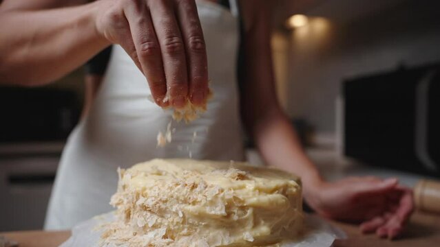 The woman sprinkles pastry crumbs on top of the Napoleon cake, covering the cream. Slow motion.