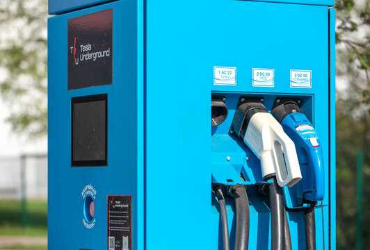 Close up view of a public fast charging station panel for electric vehicles with different plug connectors and power cables.
