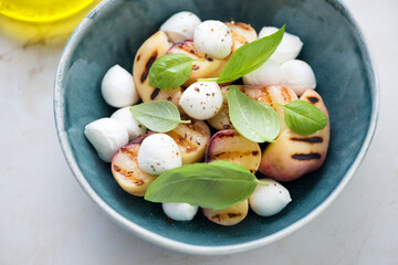 Grilled sliced peaches with baby mozzarella and fresh basil leaves in a green bowl, horizontal shot, middle closeup