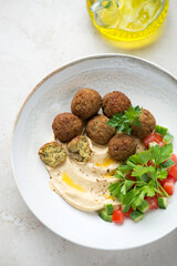Falafel with hummus, fresh greens and chopped vegetables, high angle view on a light-beige stone background, vertical shot