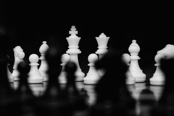 Focus on white chess pieces on the background. King and Queen with black chess pieces unfocused in front