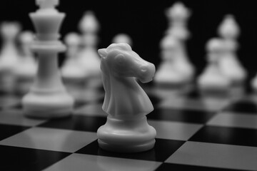 white chess knight horse in focus and chess pieces unfocused in the background