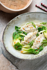 Grey bowl with dumplings and baby pok choy in a broth, vertical shot, selective focus, middle closeup
