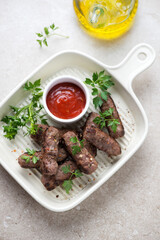 Serving tray with barbecued cevapcici or skinless beef sausages, fresh greens and dip, vertical shot on a beige stone background, high angle view