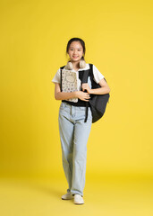 portrait of beautiful asian schoolgirl wearing a backpack on a yellow background.