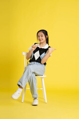 fullbody image of asian girl sitting and posing  on yellow background