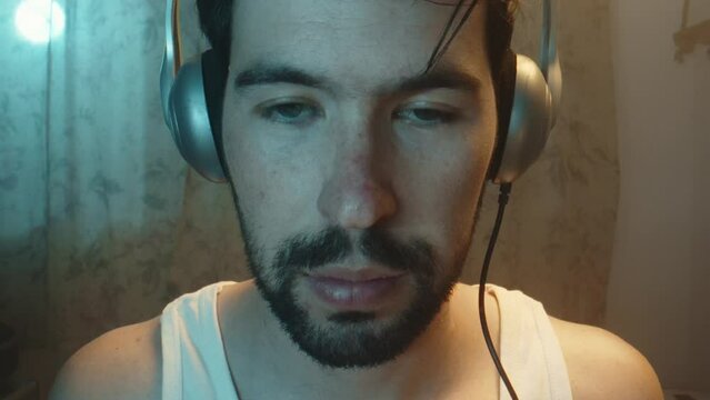 Man puts vintage headphones on head, face shows screen glare, frontal closeup