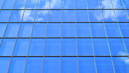 Structural glass wall reflecting blue sky. Abstract modern architecture fragment. Glass building with transparent facade of the building and blue sky. Contemporary architectural background.