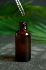 Drop of clear liquid, oil, serum or tincture dripping from pipette in the neck of a brown medical...