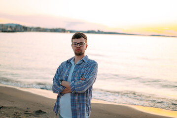 A handsome young man in glasses and a plaid shirt on the background of the sea or ocean. Travel...