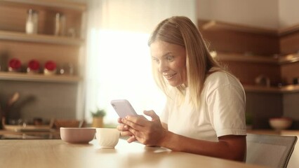 Charming mature blond woman drinking coffee while get notification on smartphone and celebrate online win success reading great news message feel amazed happy outdoors Triumph Lucky Wow concept