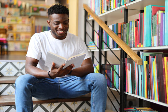Serious black man sitting on a staircase in a bookstore and reading a book. He is a young and clever student, librarian or reader who is studying, researching or learning for his university.