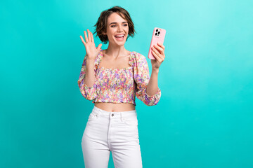 Portrait of positive girl with bob hairdo dressed flower print blouse talking on smartphone video call isolated on teal color background