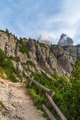 Fototapeta na wymiar .Stunning mountain view. Picturesque landscape with beautiful sharp rocks, mountains covered with forests. Trail in the mountains. Wooden fence. Dolomites, Italy.