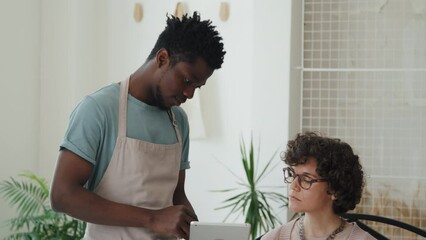 Tilt up of African American waiter holding tablet with menu talking to Caucasian woman and helping her choose something to order indoor at daytime