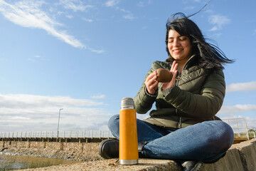 young happy latin woman smiling sitting outdoors mixing the yerba preparing mate.