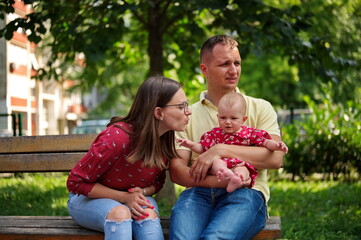 Family with little baby girl sitting on a bench in a park