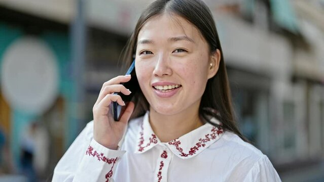 Young chinese woman talking on smartphone smiling at street