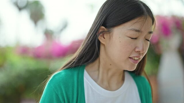 Young chinese woman looking to the side sneezing at park