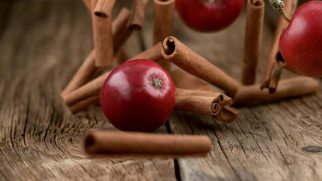 Cinnamon sticks and apples falling on wood in slow motion