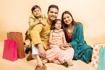 Happy young indian family wearing traditional cloths sitting together isolated on beige background,...