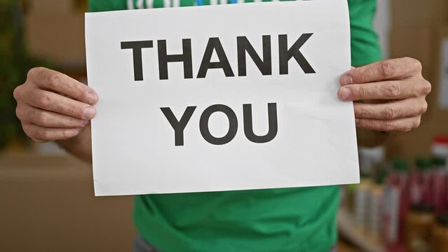 Young hispanic man volunteer holding thank you banner at charity center