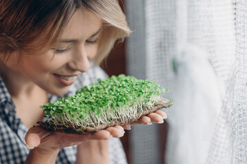 A happy woman enjoys microgreens. Close-up of a young farmer tasting his harvest. Healthy food,...