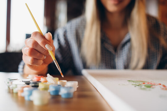 The girl enjoys painting by numbers. It is a creative hobby. Close-up. The background is blurred.