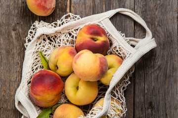 Ripe peaches in eco bag on wooden background
