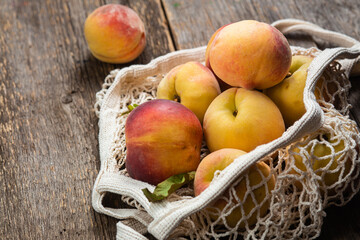 Ripe peaches in eco bag on wooden background
