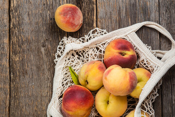 Ripe peaches in eco bag on wooden background