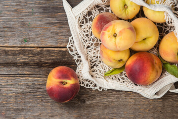 Ripe peaches in eco bag on wooden background
