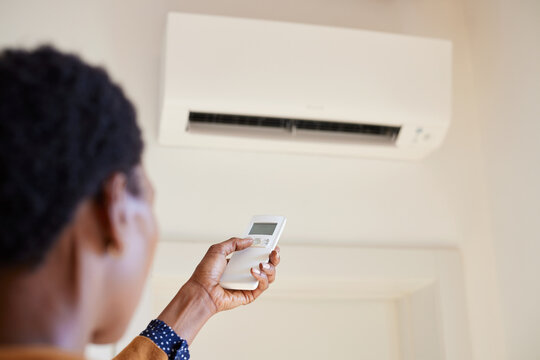 African American Woman Holding Remote Control Aimed At Air Conditioner