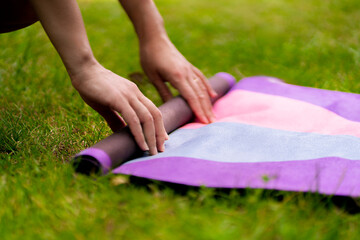 woman rolls a sport mat before a yoga class outdoors on the grass