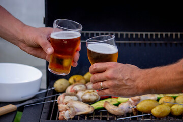 men hold beer in their hands on the background of the grill, vegetables and meat. Selective focus.