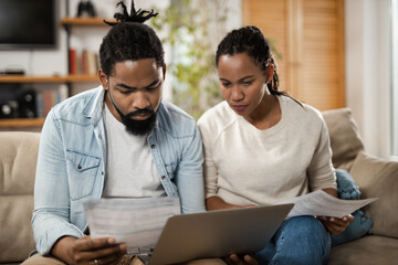 African American couple going through their financial bills while paying them over computer at home - obrazy, fototapety, plakaty