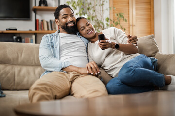 Happy African American couple watching TV on sofa in the living room