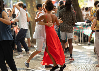 Couples dancing on the street - tanned woman wearing red bright dress in the centre