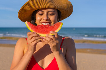Portrait of a woman eating a watermelon by the beach. Close-up smiling with bikini