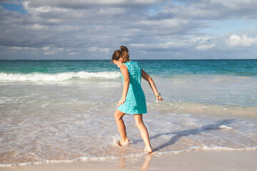 Fototapeta na wymiar Little girl in a blue dress walks the shore water on the beach