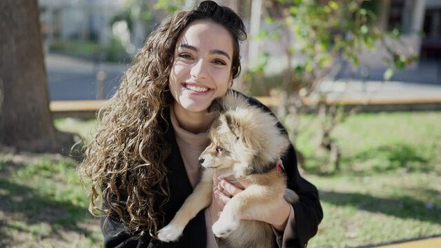 Young hispanic woman with dog smiling confident sitting on bench kissing at park