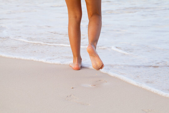 Barefoot legs of a girl walking the shore water on the beach