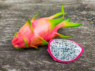Juicy pink dragon fruit with white flesh and black seeds lying on old wooden background.