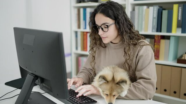 Young hispanic woman with dog student using computer studying at library university