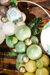 Arch decorated green, brown, golden balloons, paper palm leaves. Birthday party for girl or boy on background photo wall. Decor in style tropical zoo. Children's photo zone. Reception at party closeup