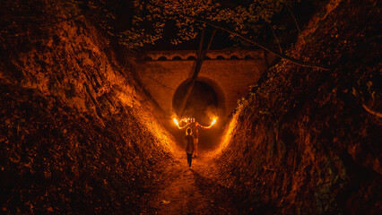 A man with torches walking through a gorge at night.