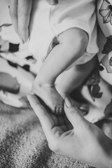 Baby feet in mom hands. Mother holding child's legs. Cute little infant lying on bed at home. Mom hold son legs. Closeup. Tiny, bare feet of newborn baby girl or boy. Sleep daughter. Black white photo