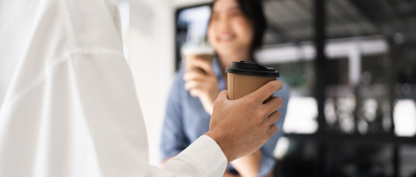 Couple of happy colleague talking while standing at the office window with cups of coffee