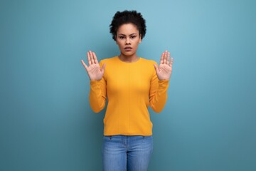 surprised young latin woman with afro hair raised her hands up showing palms on studio background